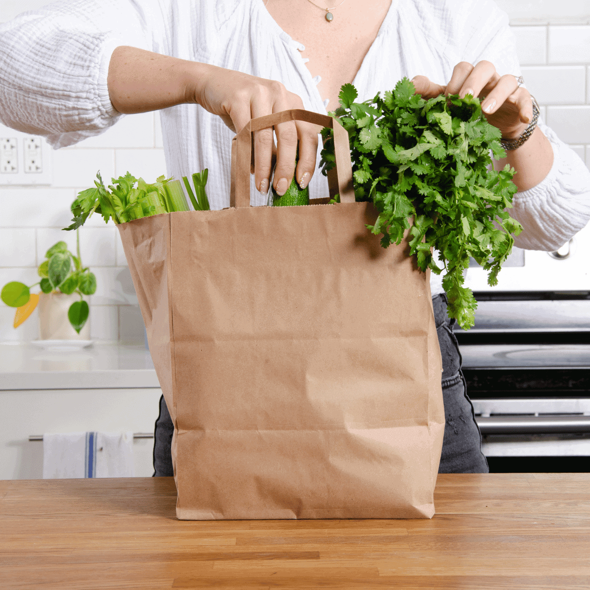 A woman grabbing fresh greens out of a paper grocery bag in a kitchen.