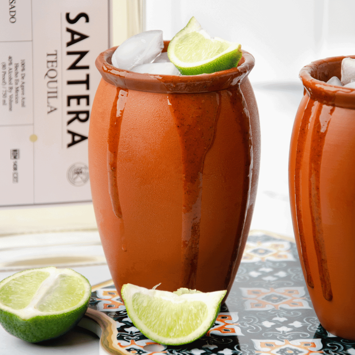 A Mexican Cantarito cocktail served in the traditional clay cup with a bottle of Santera Tequila in the background.