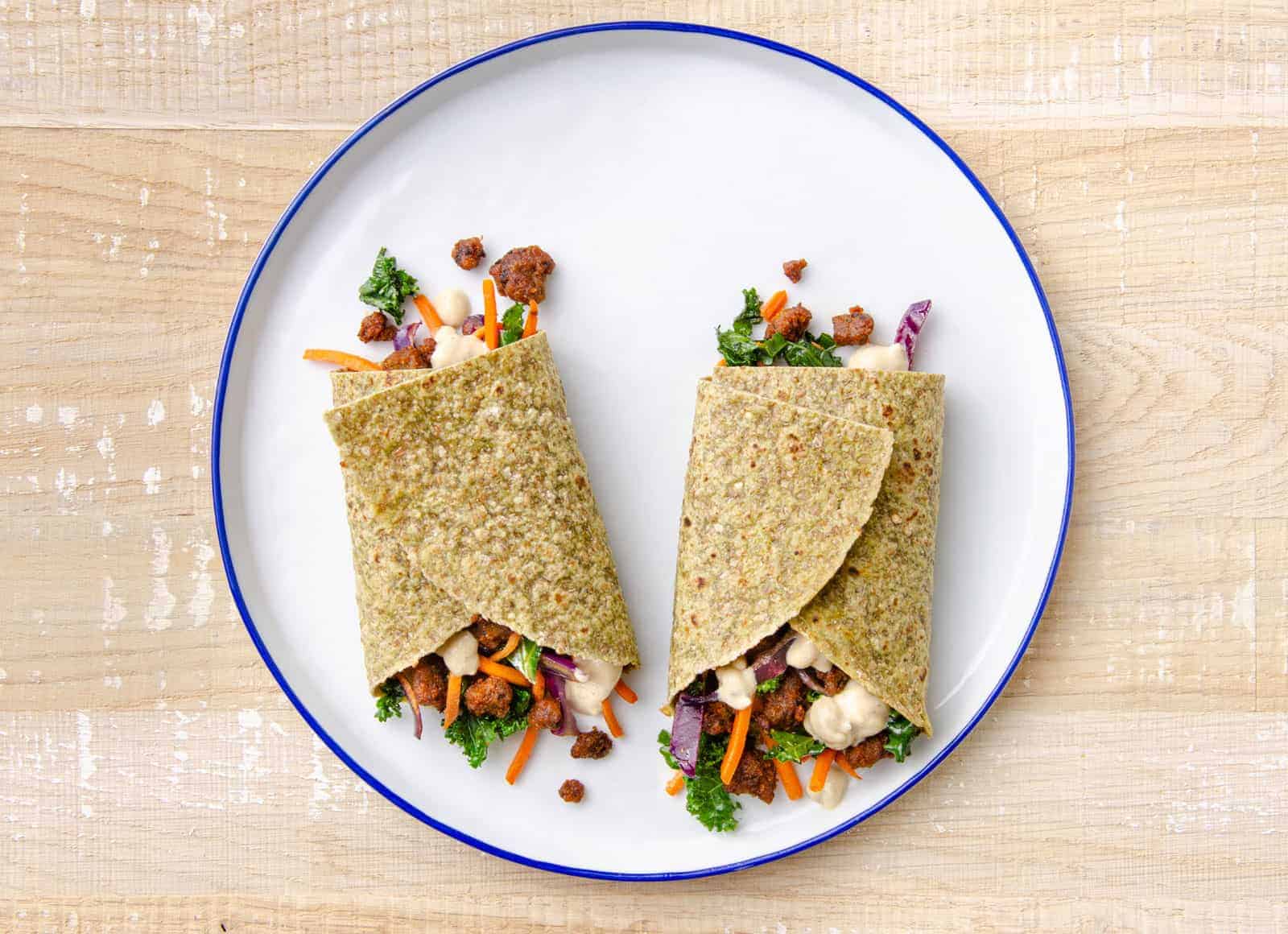 A Hungryroot vegan wrap spilling out ingredients onto a white plate sat on a wood table.